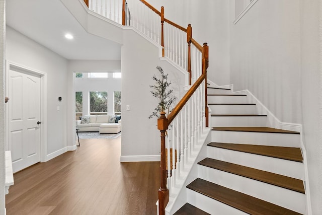 stairway with a towering ceiling, baseboards, and wood finished floors