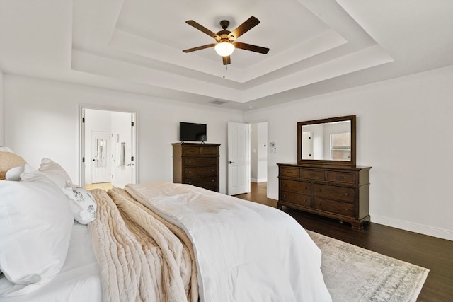 bedroom with ceiling fan, a tray ceiling, dark wood-style flooring, and baseboards