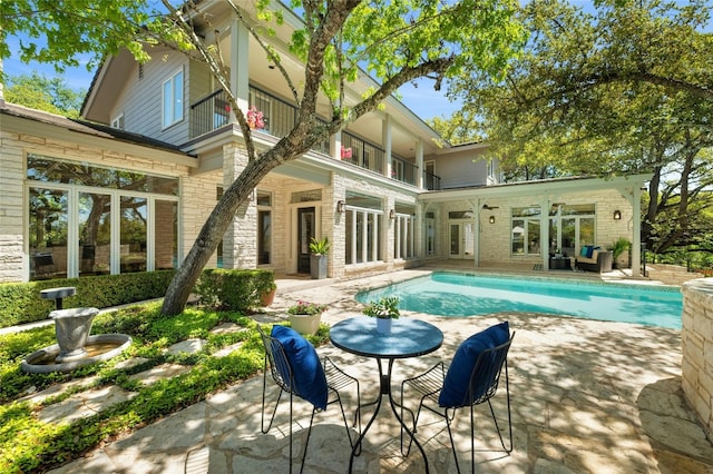 rear view of house featuring a patio, a balcony, brick siding, stone siding, and an outdoor pool