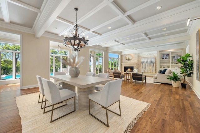 dining space featuring beam ceiling, light wood finished floors, ornamental molding, a large fireplace, and coffered ceiling