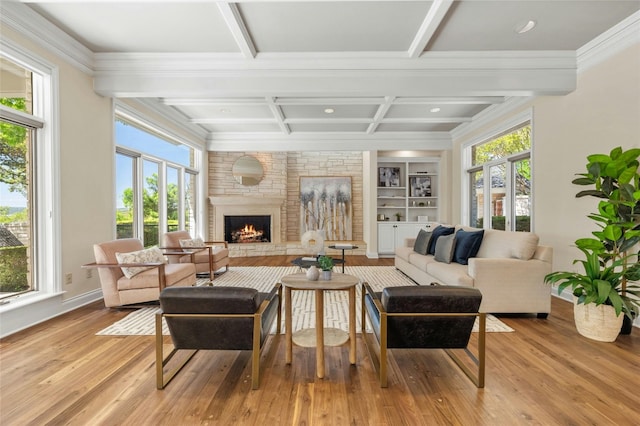 living area featuring built in shelves, beam ceiling, light wood-style flooring, a stone fireplace, and coffered ceiling