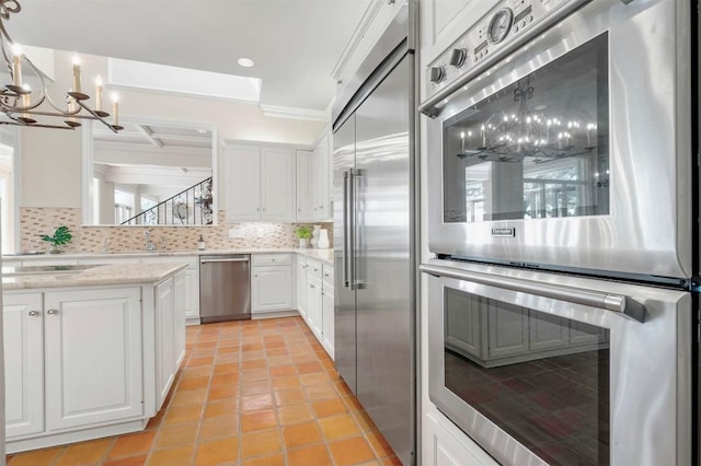 kitchen with decorative backsplash, appliances with stainless steel finishes, ornamental molding, white cabinets, and a chandelier