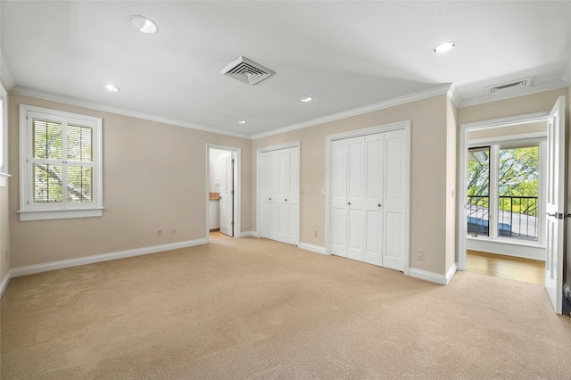 unfurnished bedroom with two closets, visible vents, ornamental molding, light carpet, and multiple windows