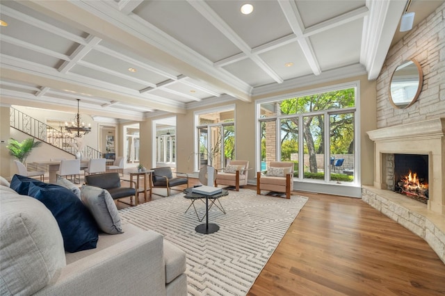 living area featuring a stone fireplace, stairway, coffered ceiling, and wood finished floors