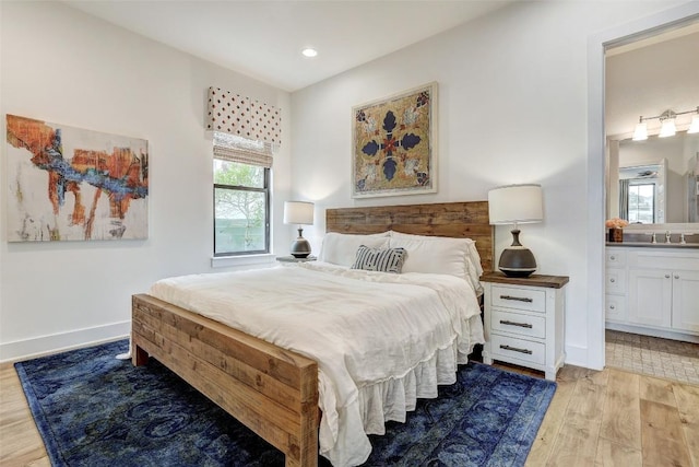 bedroom featuring baseboards, a sink, light wood finished floors, and ensuite bathroom