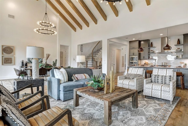 living room featuring visible vents, beamed ceiling, wood finished floors, stairs, and high vaulted ceiling