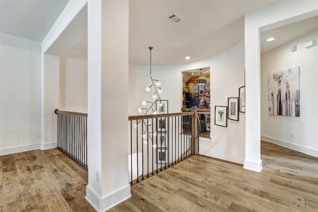 corridor with baseboards, visible vents, wood finished floors, and an upstairs landing