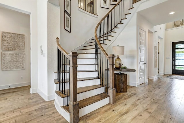 entryway with light wood-style floors, a high ceiling, baseboards, and stairs