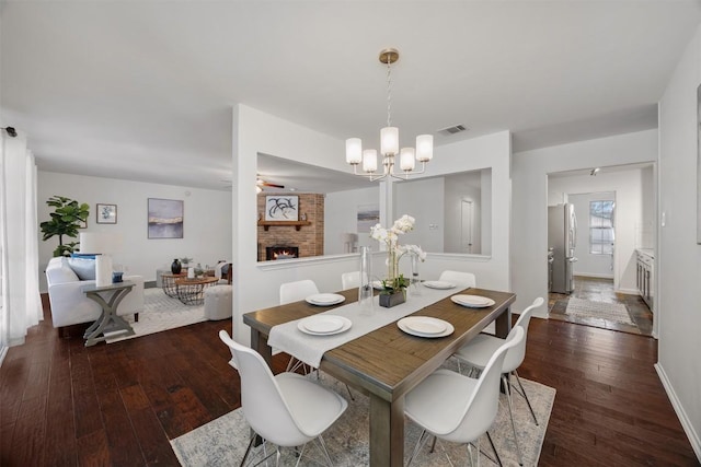 dining room featuring a brick fireplace, dark wood-style flooring, visible vents, and baseboards