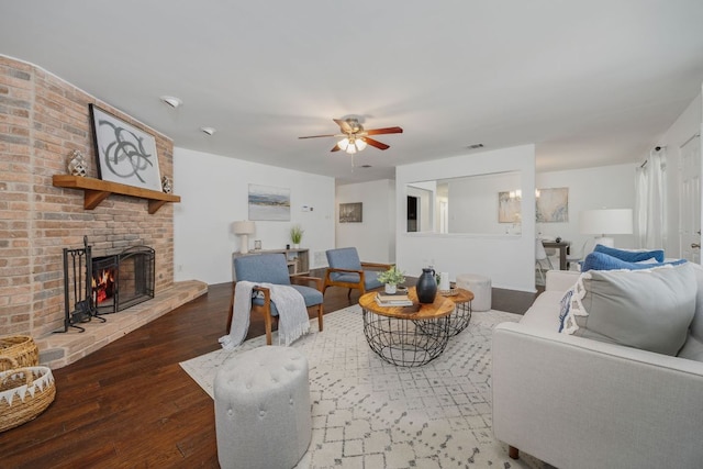 living area featuring ceiling fan, dark wood-type flooring, a brick fireplace, and visible vents