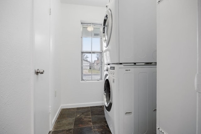 clothes washing area with laundry area, stone finish flooring, stacked washing maching and dryer, and baseboards