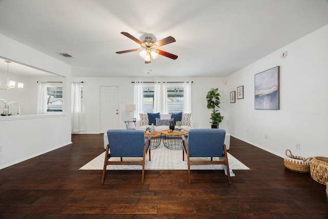 living room with visible vents, dark wood finished floors, baseboards, and ceiling fan with notable chandelier