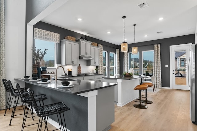 kitchen with visible vents, light wood-type flooring, under cabinet range hood, dark countertops, and a breakfast bar area