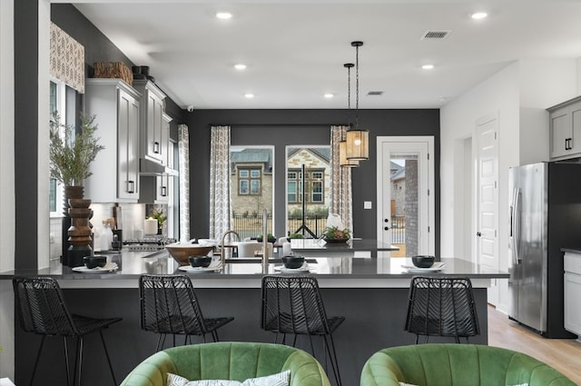 kitchen featuring visible vents, stainless steel fridge with ice dispenser, a breakfast bar, a peninsula, and hanging light fixtures