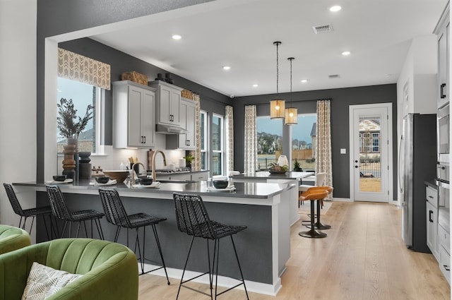 kitchen featuring visible vents, a kitchen bar, light wood-type flooring, a peninsula, and freestanding refrigerator