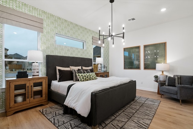 bedroom with baseboards, wood finished floors, an accent wall, and wallpapered walls