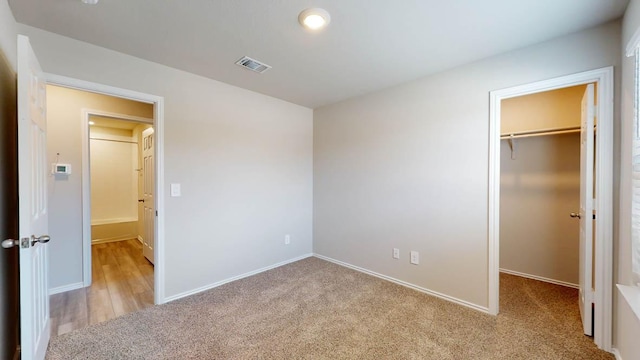 unfurnished bedroom featuring a walk in closet, a closet, visible vents, light carpet, and baseboards