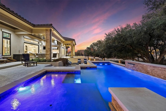 pool at dusk featuring ceiling fan, a patio, and an outdoor pool