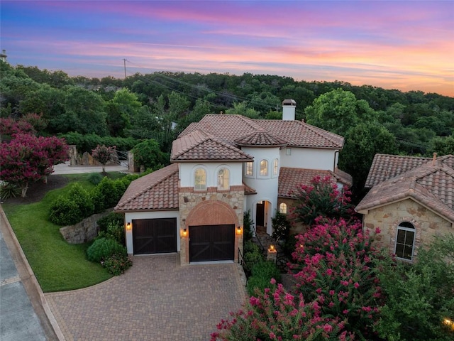 mediterranean / spanish house with stone siding, a chimney, a tiled roof, decorative driveway, and stucco siding