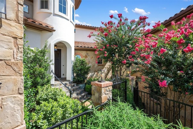 exterior space with stone siding, a tile roof, fence, and stucco siding