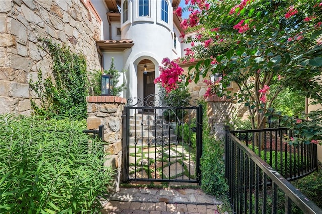 property entrance with stone siding, a gate, fence, and stucco siding