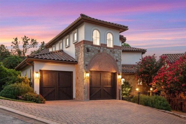 mediterranean / spanish-style house with a garage, stone siding, and stucco siding