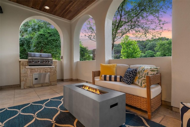 patio terrace at dusk featuring exterior kitchen, an outdoor living space with a fire pit, and grilling area