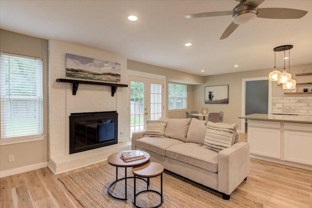 living room with ceiling fan, recessed lighting, baseboards, a brick fireplace, and light wood finished floors