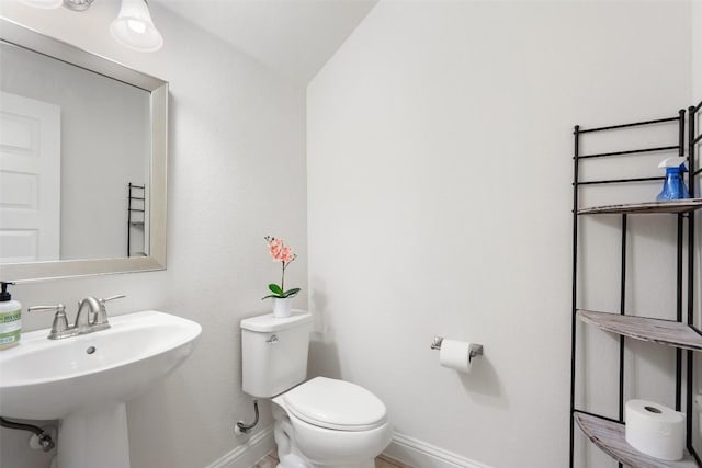 half bath with baseboards, a sink, and toilet