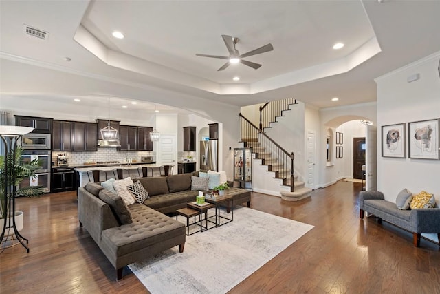 living room featuring a tray ceiling, dark wood-style flooring, visible vents, and arched walkways