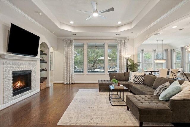 living area with ornamental molding, a tile fireplace, a raised ceiling, and wood finished floors