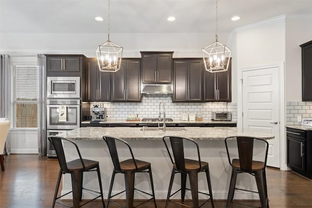 kitchen with a breakfast bar, decorative light fixtures, an island with sink, light stone countertops, and under cabinet range hood