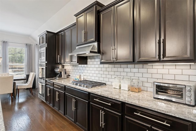 kitchen featuring a toaster, decorative backsplash, dark wood-style floors, stainless steel appliances, and under cabinet range hood