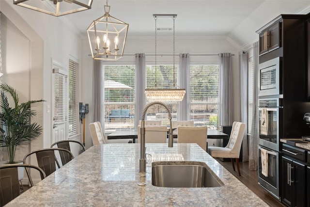 kitchen with stainless steel microwave, a sink, light stone countertops, pendant lighting, and a notable chandelier