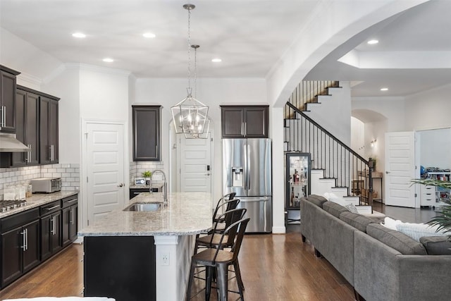 kitchen with a kitchen island with sink, stainless steel appliances, a sink, open floor plan, and pendant lighting