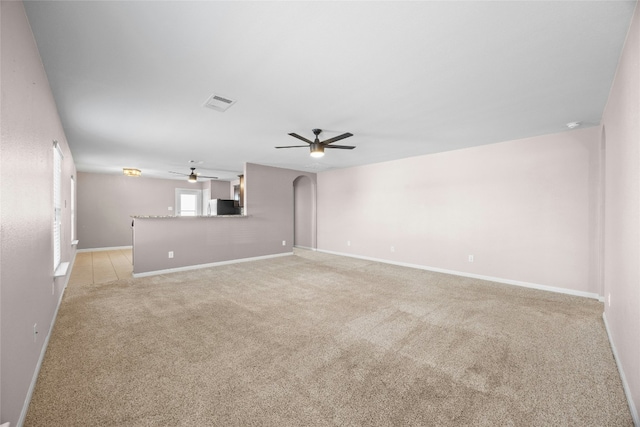 unfurnished living room with arched walkways, light colored carpet, ceiling fan, and baseboards