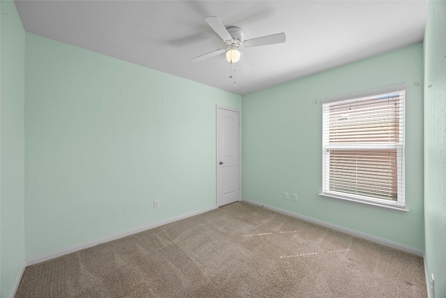 spare room with light carpet, a ceiling fan, and baseboards