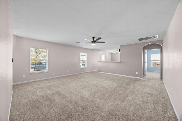 empty room featuring light carpet, a wealth of natural light, arched walkways, and visible vents