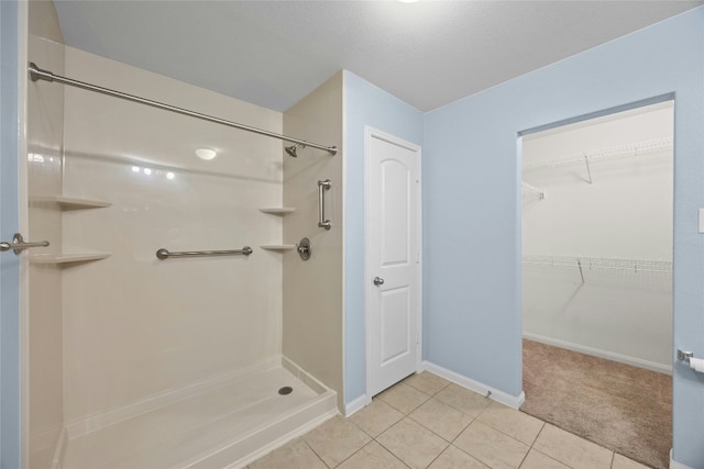 bathroom with baseboards, a spacious closet, a shower stall, and tile patterned floors