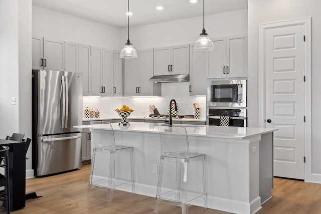 kitchen with a center island with sink, appliances with stainless steel finishes, light countertops, and a kitchen breakfast bar