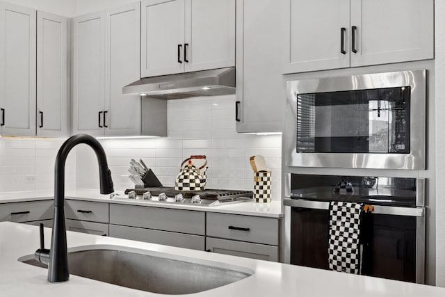 kitchen featuring a sink, stainless steel appliances, light countertops, and under cabinet range hood