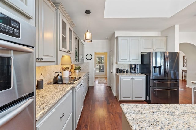 kitchen featuring stainless steel appliances, hanging light fixtures, dark wood-type flooring, glass insert cabinets, and light stone countertops