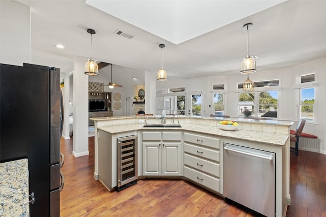 kitchen featuring stainless steel appliances, open floor plan, a kitchen island with sink, a sink, and beverage cooler