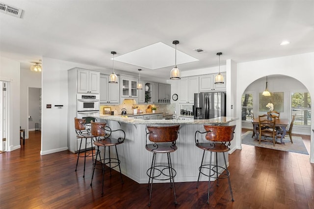 kitchen featuring stainless steel fridge, glass insert cabinets, light stone countertops, gray cabinetry, and pendant lighting