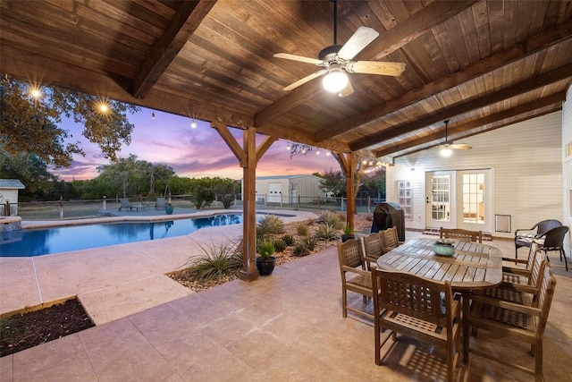 patio terrace at dusk with a fenced in pool, area for grilling, ceiling fan, fence, and outdoor dining area