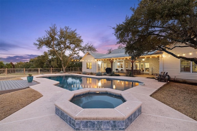 pool at dusk with an in ground hot tub, a patio area, fence, and a fenced in pool