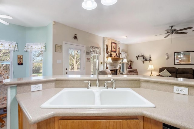 kitchen featuring a ceiling fan, open floor plan, a sink, and a stone fireplace