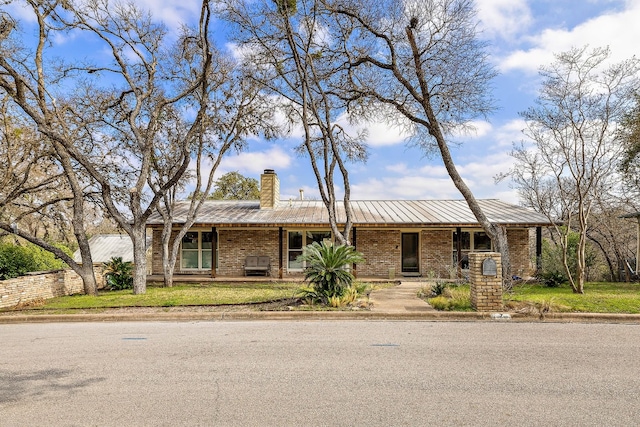 view of front of property featuring brick siding, metal roof, a chimney, and a front lawn