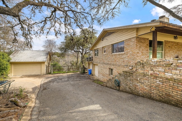 view of property exterior featuring an outbuilding, brick siding, a detached garage, and fence