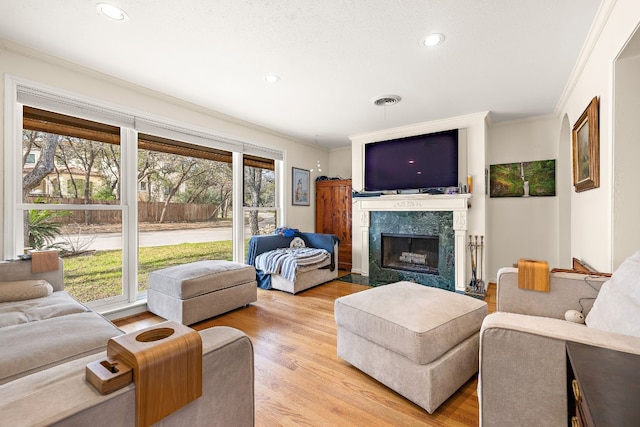 living room with light wood-style floors, a premium fireplace, visible vents, and crown molding